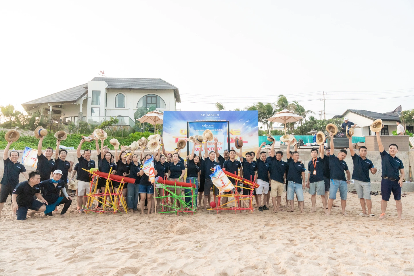 Tập thể nhân viên AB Mauri giơ cao mũ cói trong hoạt động teambuilding trên bãi biển