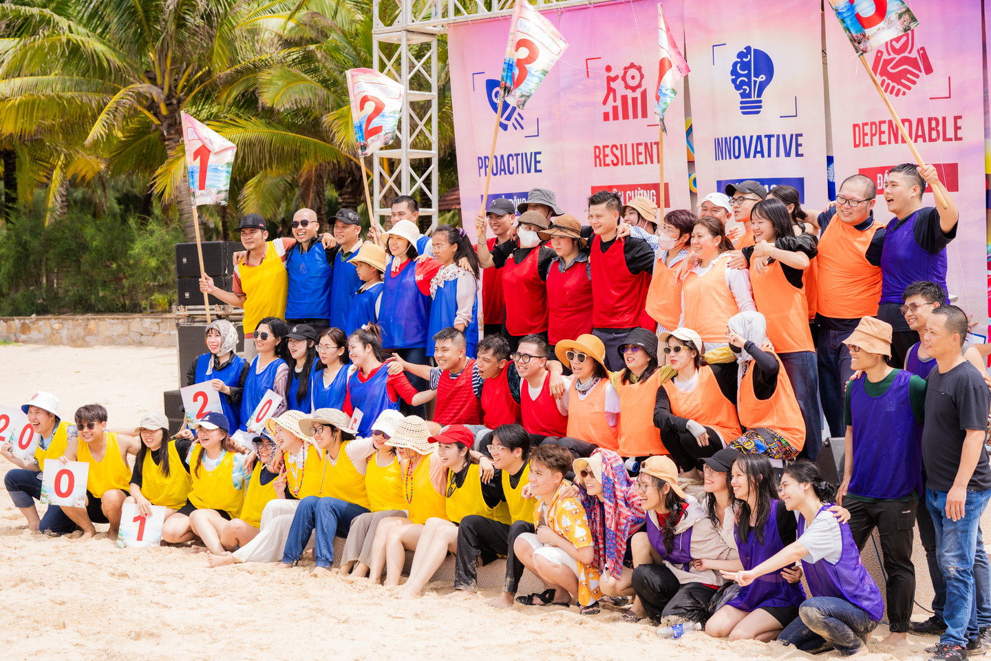 Tập thể nhân viên mặc áo đồng đội nhiều màu sắc chụp ảnh kỷ niệm trong buổi team building trên bãi biển