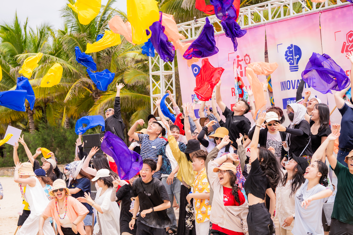 Nhóm bạn trẻ hào hứng tung những dải lụa màu sắc lên không trung trong một hoạt động teambuilding ngoài trời