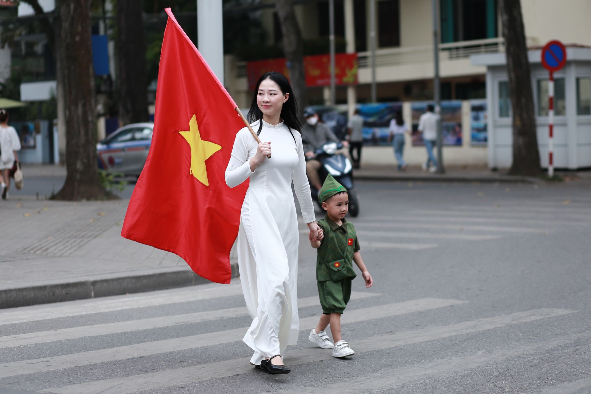 PhPhụ nữ mặc áo dài và em nhỏ cầm Quốc kỳ trên phố Hà Nội